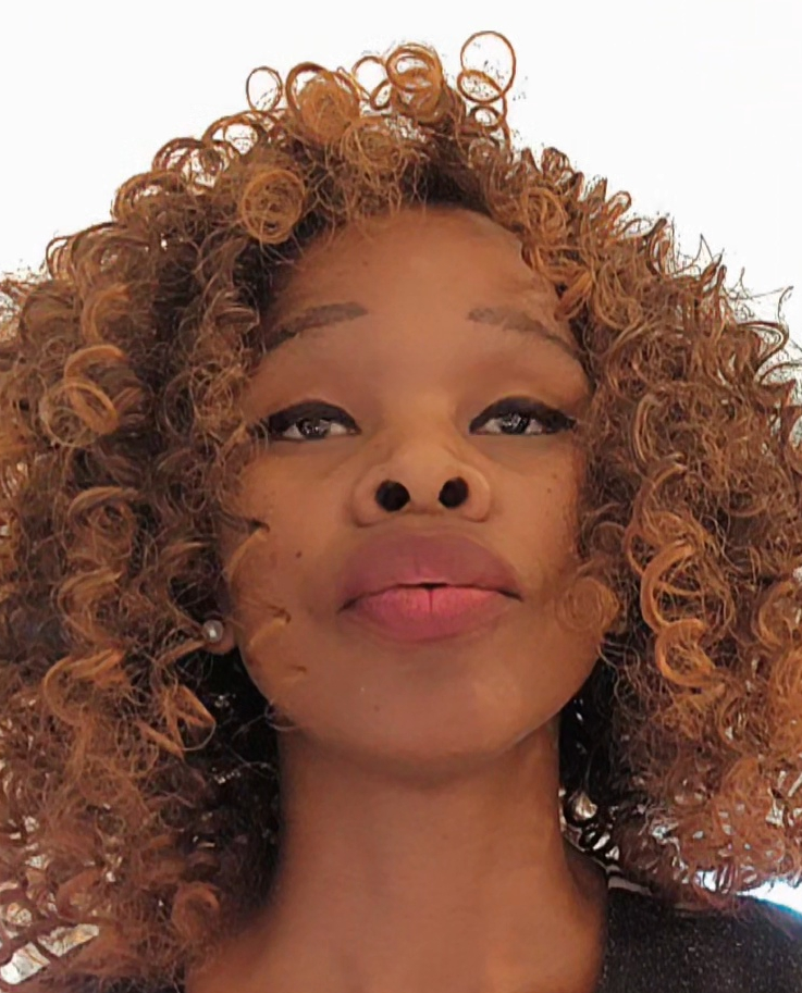 Close-up portrait of a woman with curly hair and natural makeup, looking directly at the camera.